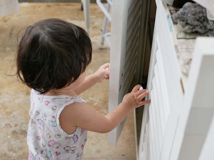 Selective focus of little curious Asian baby girl's hands open a cabinet of daddy's mechanic tools -...