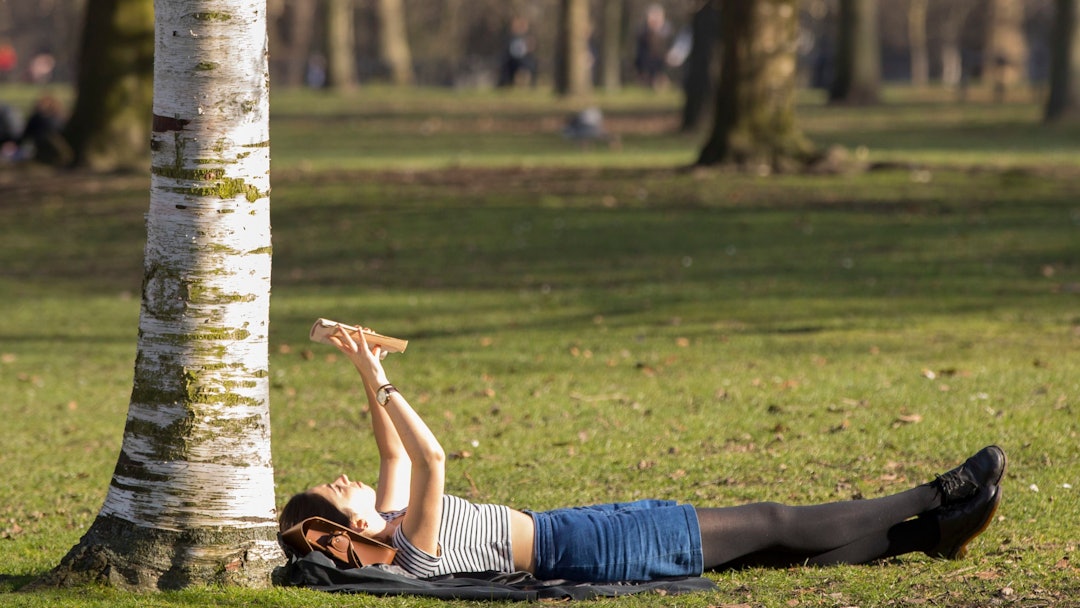 A woman enjoys reading her book in the sunshine in Hyde Park on what is set to be the warmest day in...