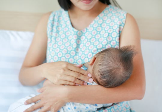 Mother breastfeeding her newborn child on the bedroom.