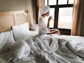 Beautiful happy young woman drinking coffee or tea in bed in hotel room or home bedroom. Stylish  br...