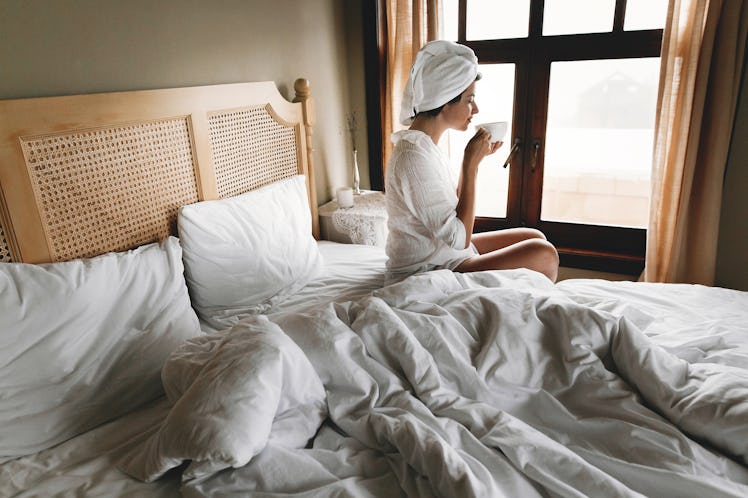 Beautiful happy young woman drinking coffee or tea in bed in hotel room or home bedroom. Stylish br...