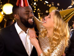 Glad mixed-race couple in party hats celebrating birthday, holiday entertainment