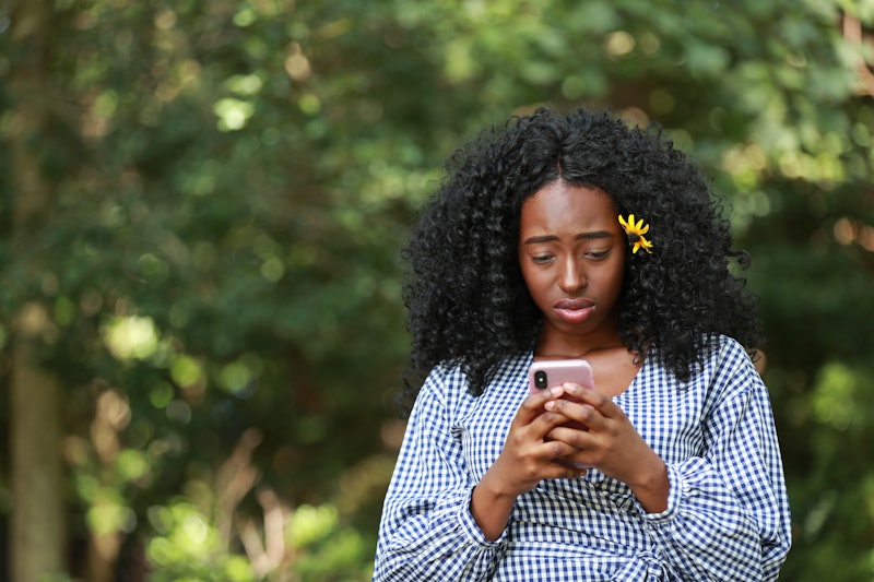 Young disappointed African American woman texting in sunny park 