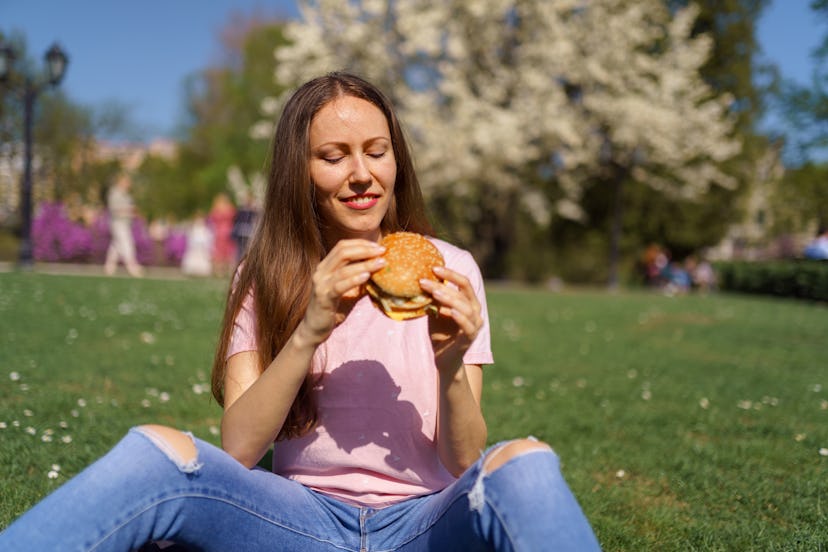 Successful business woman eating fast food burger cheesburger enjoys her leisure free time in a park...