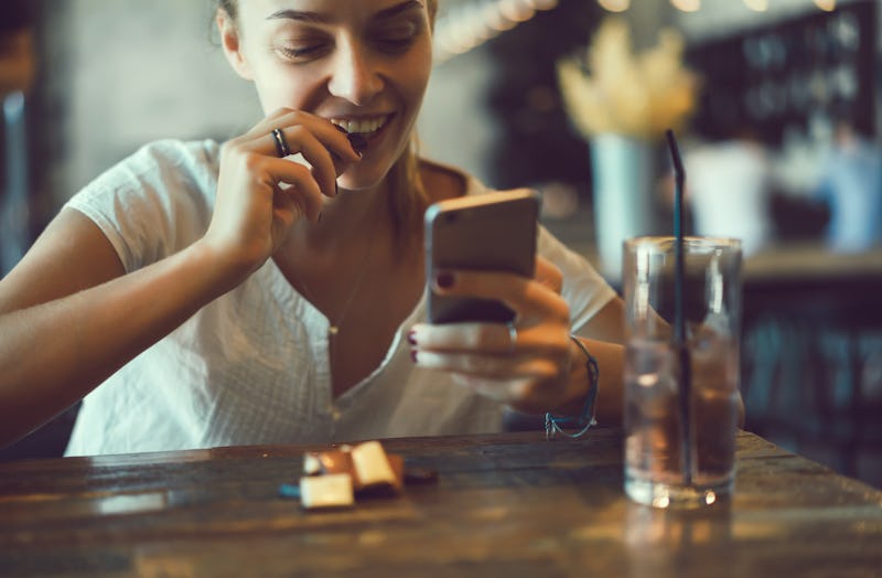 young pretty brunette woman eat chocolate in cafe, using smartphone, touch screen display, sweet foo...