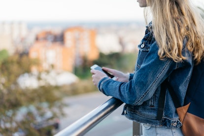 young millennial girl in a jeans jacket use smartphone, city blurring on background, space for text....