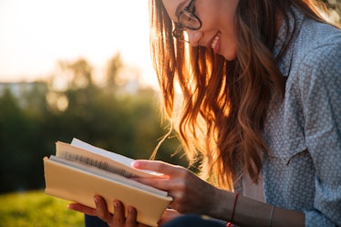Cropped image of smiling brunette woman in eyeglasses reading book in park