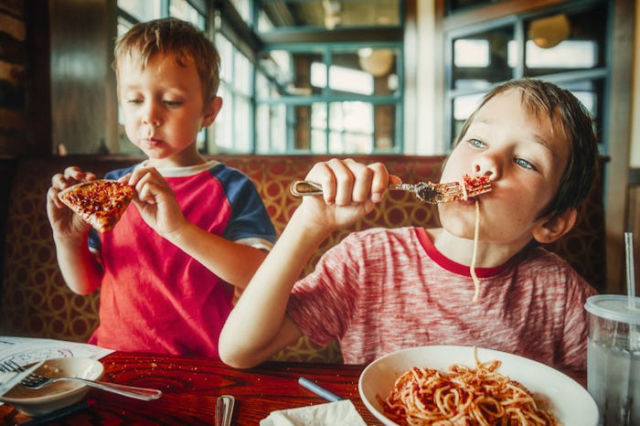 kids eat pizza and pasta at cafe. children eating unhealthy food indoors