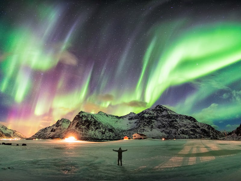Aurora borealis (Northern lights) over mountain with one person at Skagsanden beach, Lofoten islands...