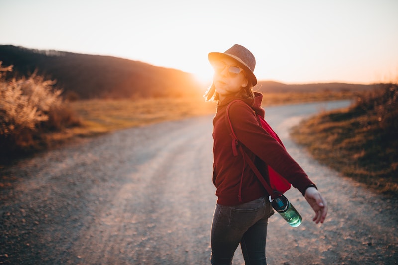 Happy girl wearing backpack and hat hiking alone during sunset