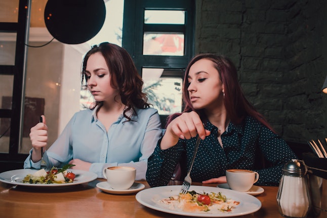 Two unhappy lesbians not talking to each other after having quarrel during lunch at coffee shop: sad redhead woman feeling lonely while her girlfriend sitting next to her.