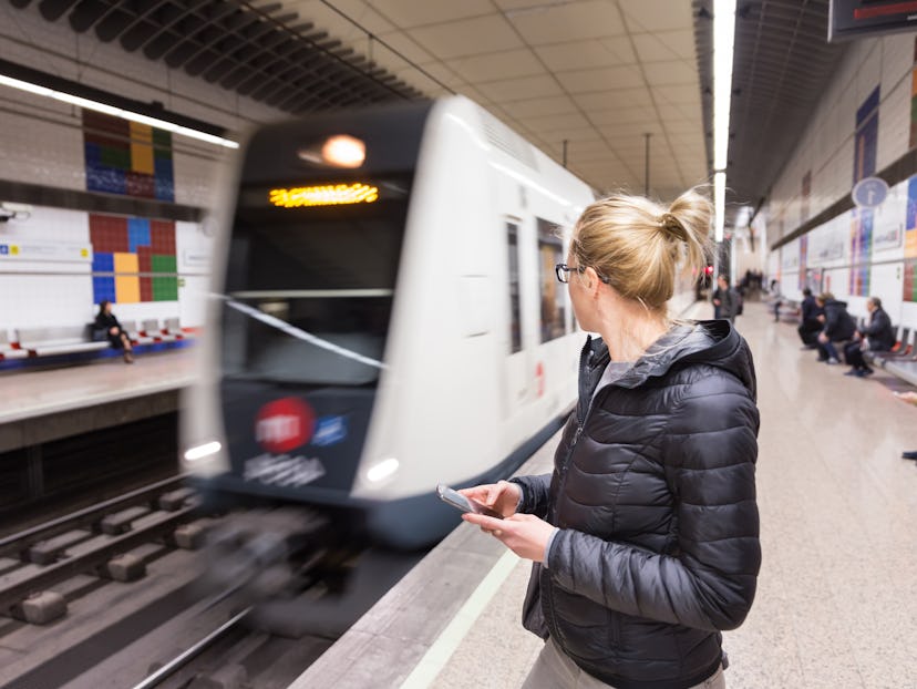 Young casual woman with a cell phone in her hand waiting on the platform of a metro station for metr...