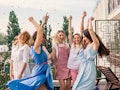 A group of women party and dance in the sunshine on a balcony celebrating a bachelorette party.