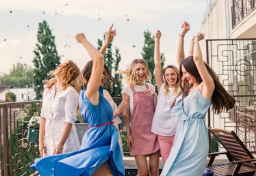 A group of women party and dance in the sunshine on a balcony celebrating a bachelorette party.