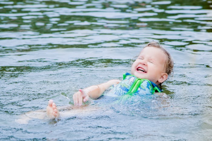 A one year old little girl floats on her back while wearing a life jacket and swimming in a Michigan...