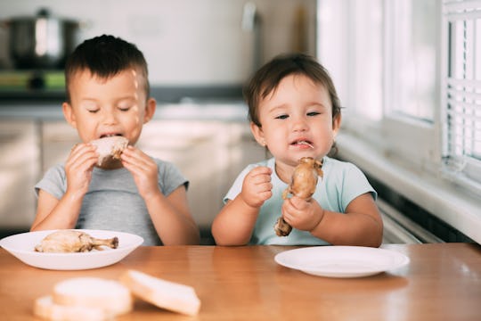Kids boy and girl , brother and sister in the kitchen having fun and eating chicken with appetite is very cute