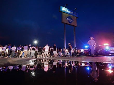 A State Trooper walks past a water puddle while people stand around the make shift memorial at the s...