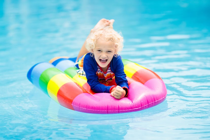 Happy child on inflatable ice cream float in outdoor swimming pool of tropical resort. Summer vacati...
