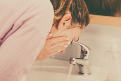 Woman cleaning washing her face with clean water in bathroom. Girl taking care of her complexion. Mo...