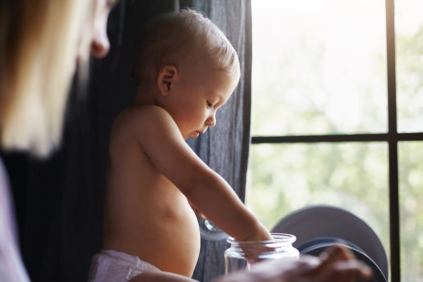 Cropped shot of unrecognizable blonde female sitting at window watching her cute baby infant explore...