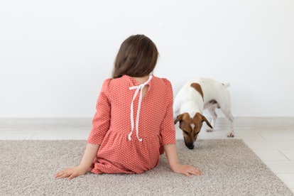 Rear view of a little girl in a red polka dot dress sitting on the floor next to her beloved dog Jac...
