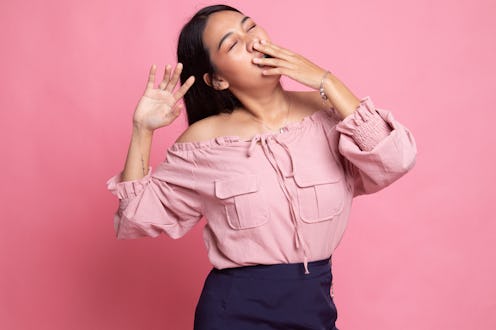 Sleepy young Asian woman yawn on pink background