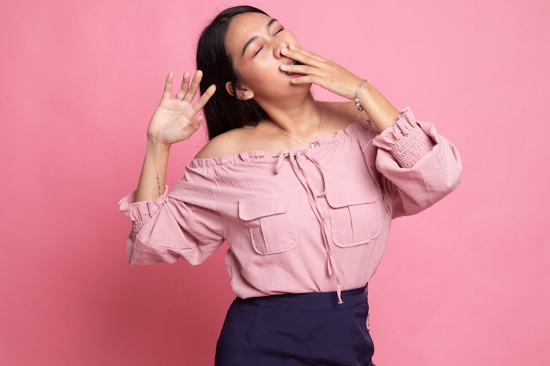 Sleepy young Asian woman yawn on pink background