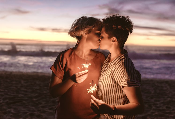 Affectionate young lesbian couple holding sparklers and kissing while enjoying a romantic moment at ...