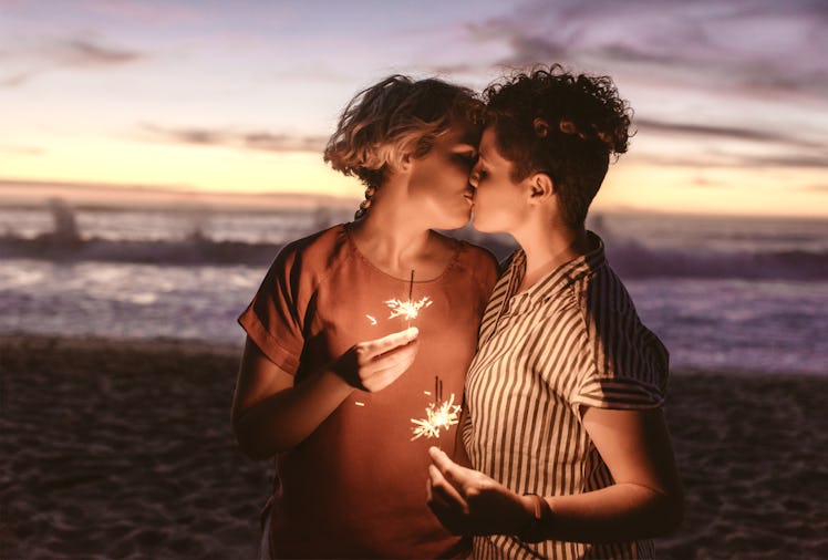 Affectionate young lesbian couple holding sparklers and kissing while enjoying a romantic moment at ...