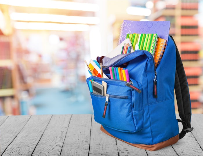 Open blue school backpack on withe table in library background.