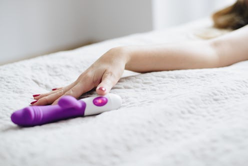 Young woman's hand reaching for sex toy dildo in bed