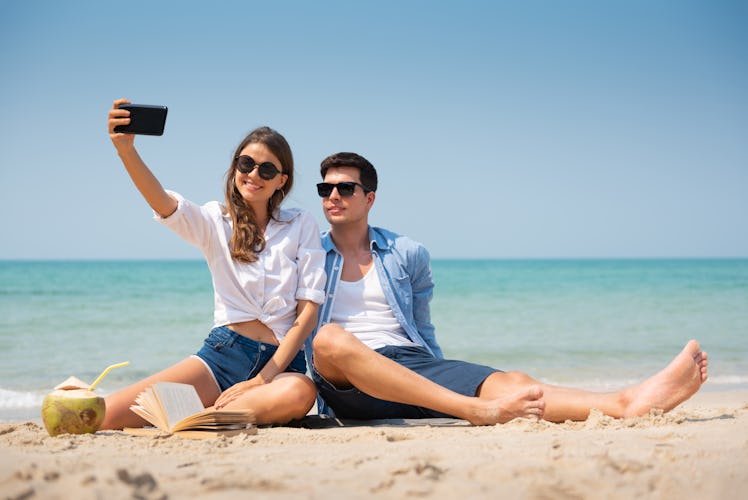 Smiling Young couple in casual clothes and sunglasses taking a selfie on the beach with copy space.