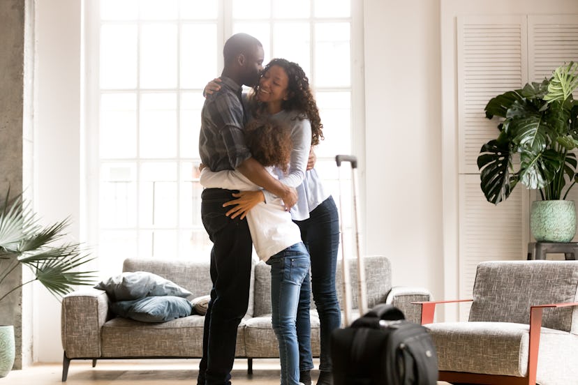 Happy black family embrace together in living room meeting welcoming african dad coming home after b...
