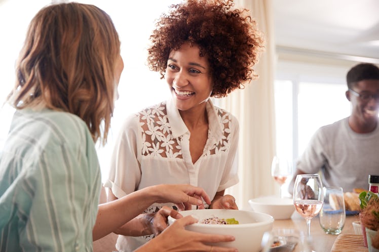 Two millennial girlfriends talking at the table during lunch with friends, close up