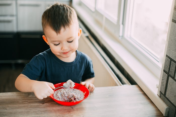 A child in the kitchen eating their own oatmeal with a red plate