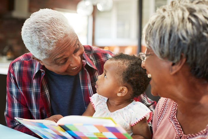 Grandparents Reading Book With Baby Granddaughter At Home