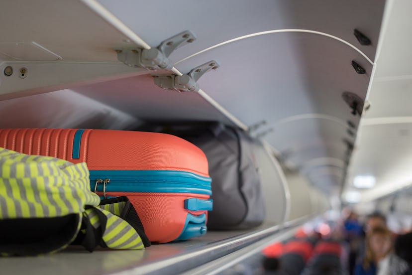 Carry-on luggage on the top shelf over head on airplane, passenger put bag cabin compartment air cra...