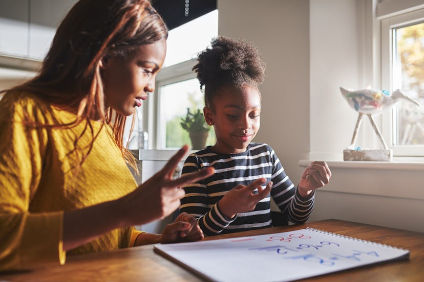 Patient mom teaching daughter schoolwork at home, black family