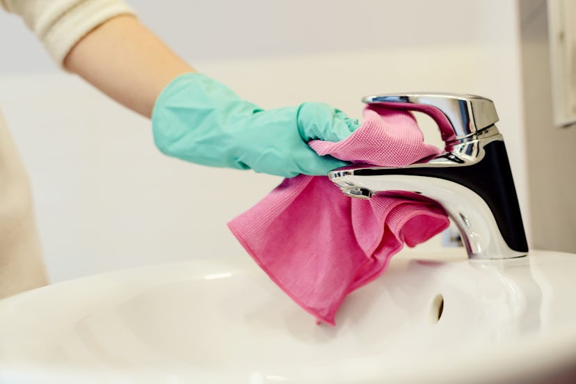 Female hands with green rubber protective gloves cleaning tap with pink cloth. Spring cleaning