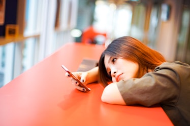 Lonely sad girl lying down on the table waiting for text message from phone