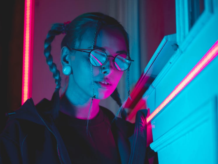 Young pretty girl with unusual hairstyle near glowing pink and blue neon lights of the city at night...