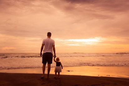 Father and little daughter standing on beach at sunset. Dad and baby girl near sea