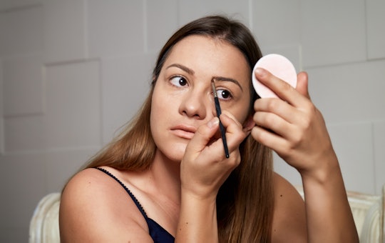 Young woman applying eyebrows make-up. Beautiful woman applying eyeshadow on her eyebrow with brush....