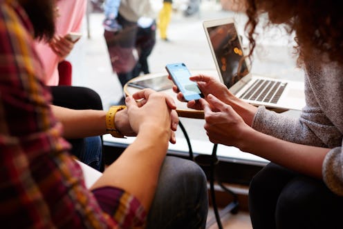 Closely image of woman is making an on-line purchase via cell telephone, while is sitting with frien...
