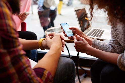 Closely image of woman is making an on-line purchase via cell telephone, while is sitting with frien...