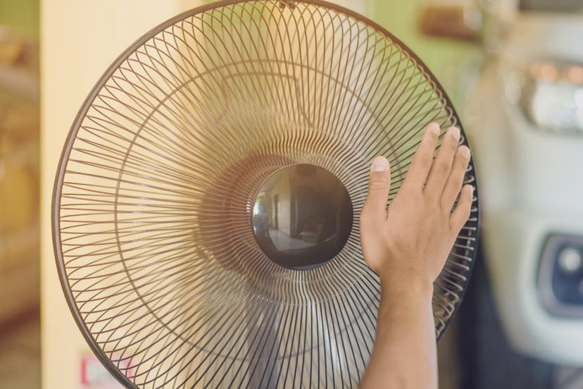 Hand of Young man touch and adjust  on front grills of electric fan for a good wind in his home in s...