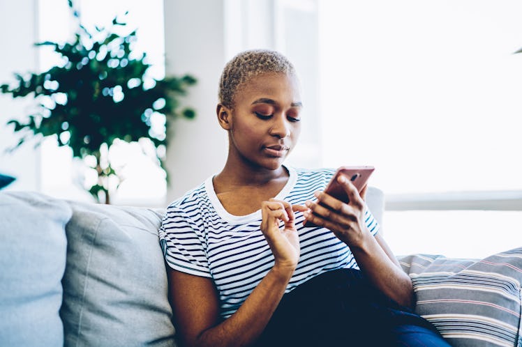 Pensive african american hipster girl making banking via application on smartphone while sitting on ...