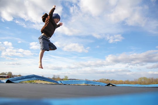 A young child is jumping high while playing outside in the yard on a large, dangerous family trampol...