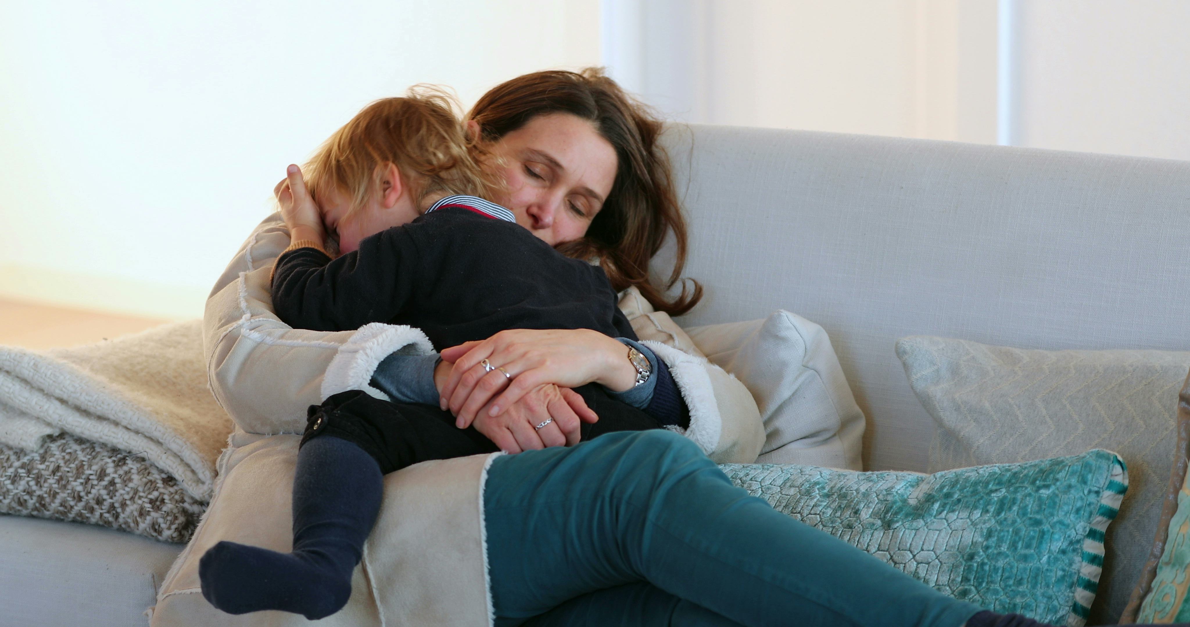 Candid authentic real life family scene with mom and toddler son together in living room sofa about ...