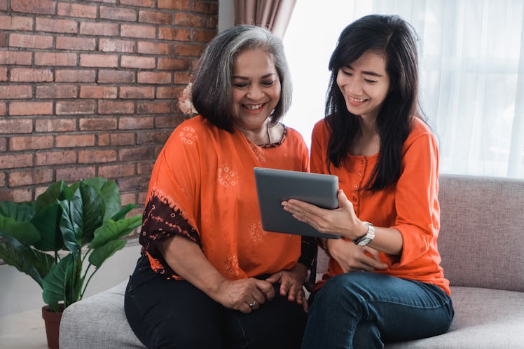 Beautiful senior mom and her adult daughter are using a digital tablet and smiling while sitting on ...